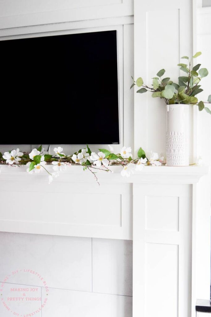 A photo of a TV mounted on the wall with a spring-themed mantel decoration.
