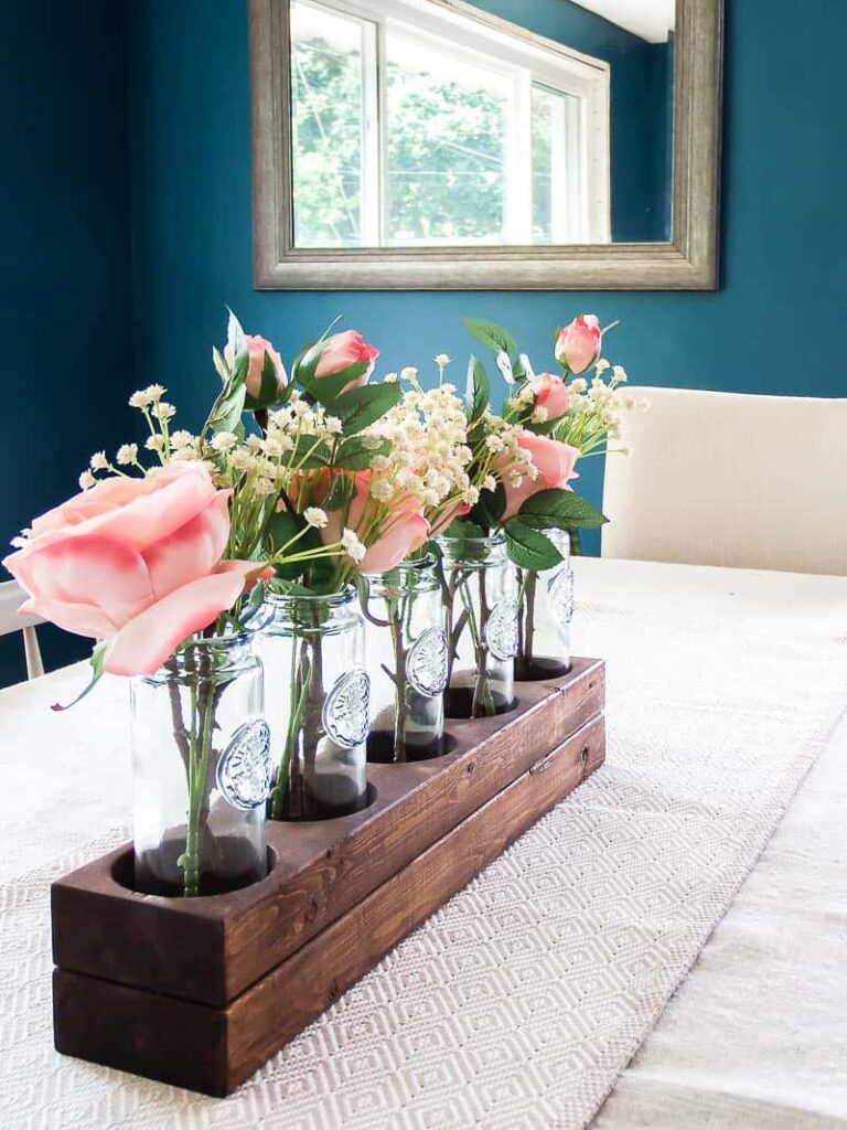 A photo of five bottles used as spring décor, with a flower, displayed on a kitchen table.
