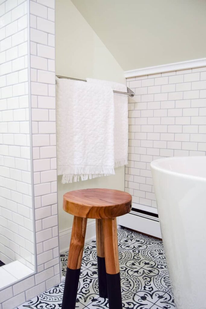 Polished chrome double towel rack with white towels next to a soaker tub with black and white patterned tile flooring with a wooden stool 