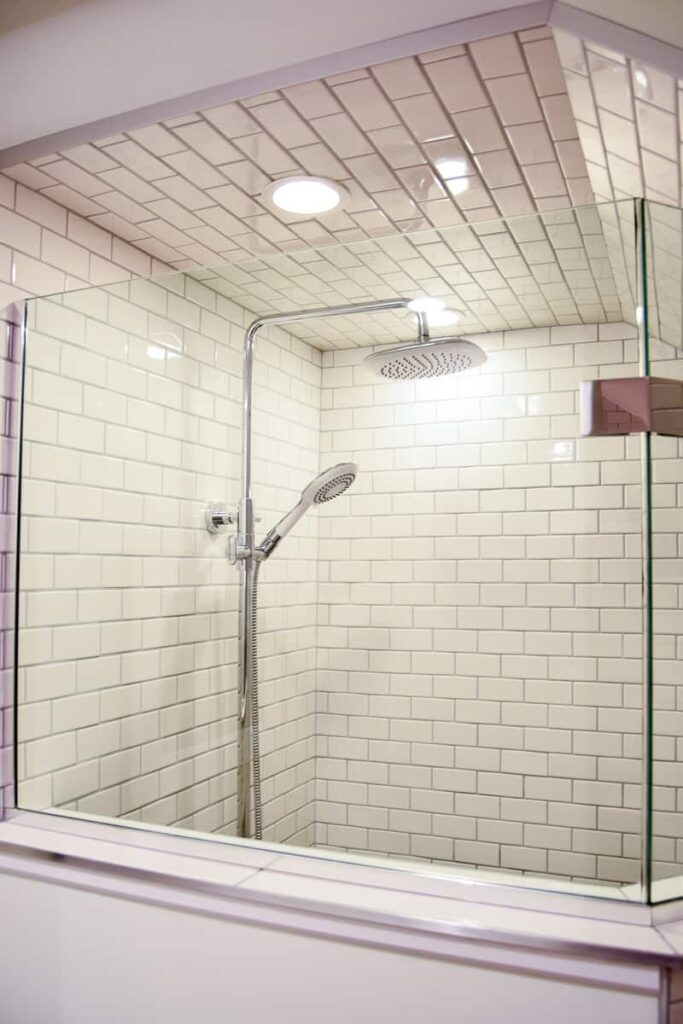 bathroom with shower with subway tile and polished chrome shower head behind a clear glass shower door 