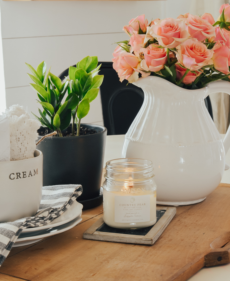 A photo of spring décor featuring candlelights and flower-filled pots on a table.
